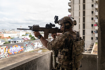 Fototapeta premium Tactical special force soldier aiming sniper weapon near window edge during urban military training operation in building
