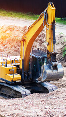 Yellow heavy duty excavator earthmoving machine parked on construction site with dirt piles and green grass under bright sun light lens flare. Vertical photo © HENADZY