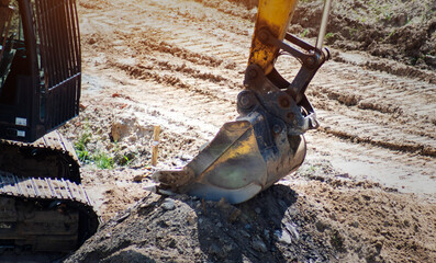 Excavator bucket resting on mound of excavated earth at construction site, heavy machinery arm and tracks visible, ground disturbed by digging, daytime outdoor work © HENADZY