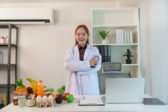 Asian female nutrition consultant standing in office with healthy food on desk for dietary wellness