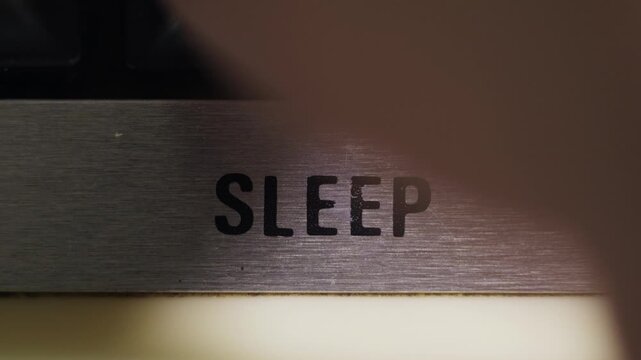 Finger presses a black SLEEP button on a silver panel for rest standby and power saving concepts