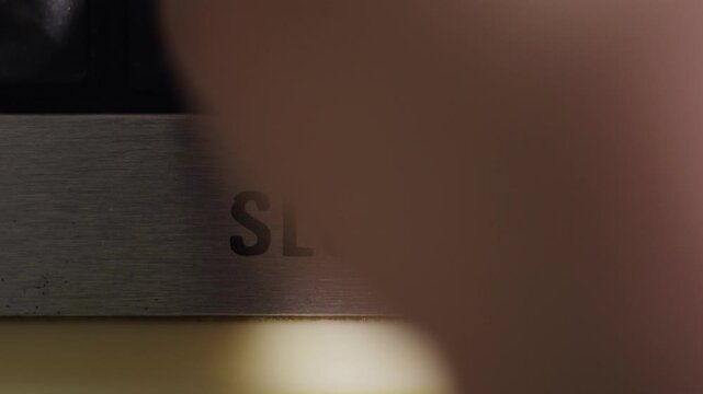 Finger presses a black SLOW button on a silver panel for reduced speed patience and caution concepts