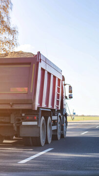 Rear view of massive red dump truck transporting sand on open road under clear sky, showcasing heavy duty vehicle vital for cargo transportation logistics vertical photo