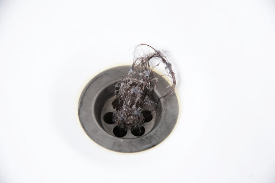 Clump of dark hair and soap residue on white sink drain, close-up view of bathroom plumbing problem, unhygienic accumulation of organic waste causing blockage, copy space