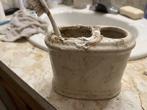 Toothbrush holder sits on a dirty bathroom vanity counter near a sink.