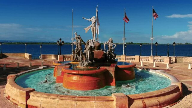 4K pan left drone shot of Raices Fountain at Paseo de la Princesa, Old San Juan, PR. Shows fountain and Atlantic Ocean view. For tourism, culture, real estate.