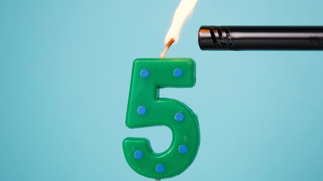 Number five birthday candle being lit with a lighter on a blue background. Fifth birthday party celebration concept. High quality 4k footage