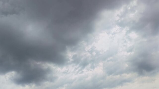 Static shot of dark storm clouds slowly moving across a dramatic sky with soft light breaking through the cloud cover.