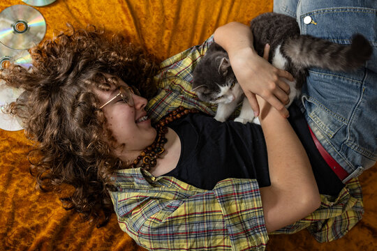 Smiling teenage girl hugs a cat while lying on a yellow blanket