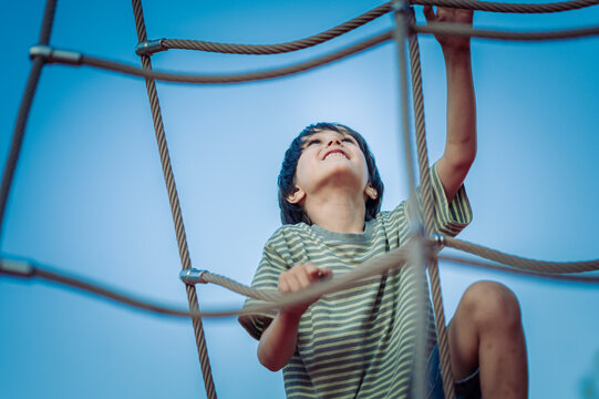Smiling boy climbing a rope net on a playground obstacle course
