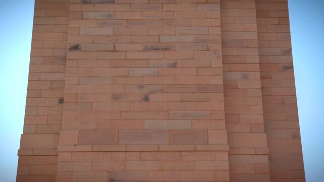 Camera tilting up along the red sandstone pillar showing engraved names of fallen soldiers at India Gate war memorial in New Delhi, India.