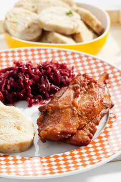 Plate of pork knucke with slices of bread dumpling and red cabbage in wooden tray, close up