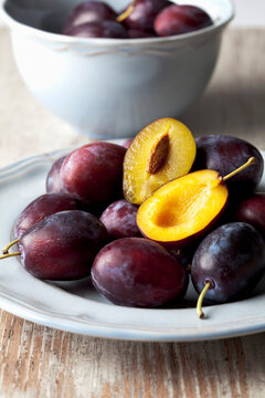 Plate and bowl with plums (Prunus domestica) on wooden table, studio shot