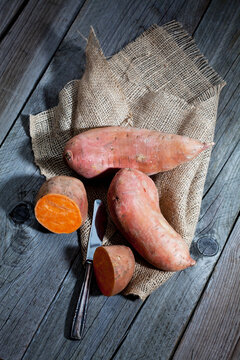 Row sweet potatoand knife on jute, wood