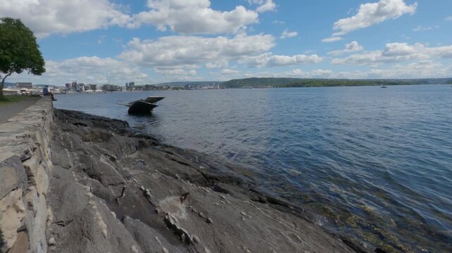 Tilt up shot from slate rocks to reveal blue fjord water and promenade wall