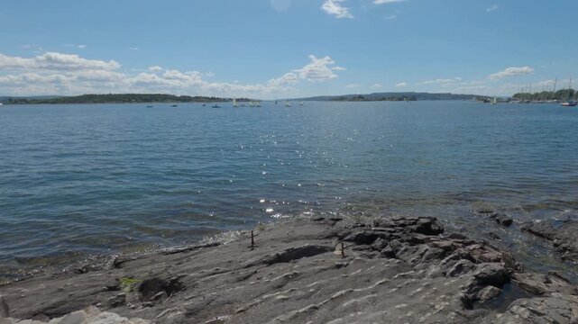 Wide view of slate rocks on shoreline washed by calm sparkling sea water