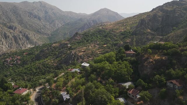 4K 10-bit drone shot flying low and forward over a lush green village with traditional houses on a sunny day in Kemaliye, Turkey