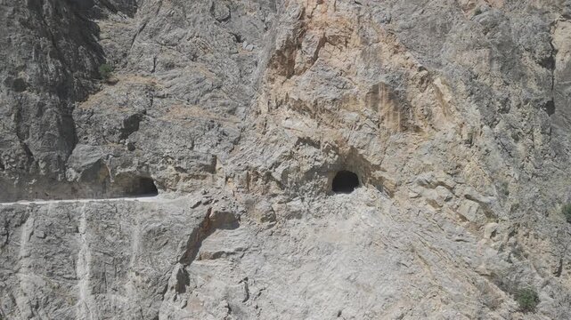 4K 10-bit cinematic drone strafe shot flying laterally in front of giant cliff walls showing hand-carved stone tunnel windows in Dark Canyon, Turkey