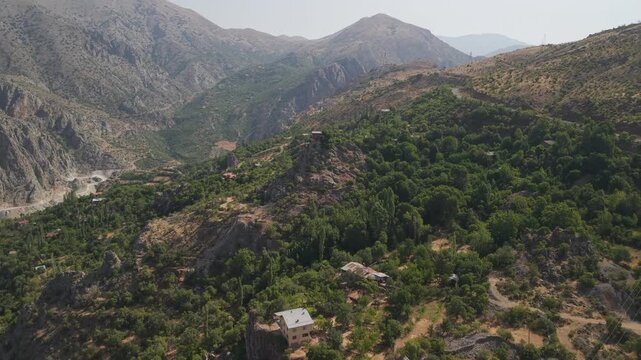 4K 10-bit drone shot flying low and forward over a lush green village with traditional houses on a sunny day in Kemaliye, Turkey