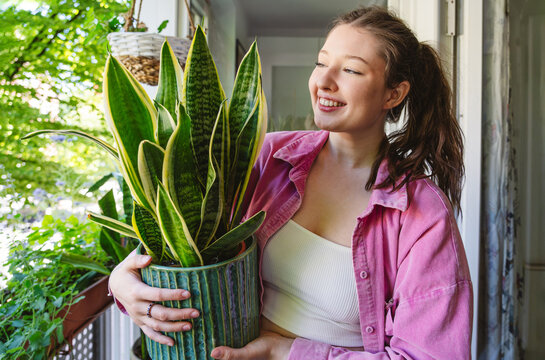Smiling woman holds a potted sansevieria plant on a balcony