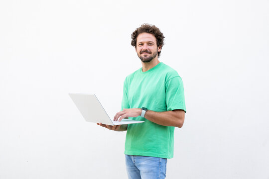 Smiling man uses laptop while standing against white background