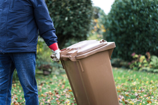 Man pulls a brown waste bin through an autumn garden