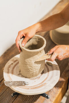 Female potter shapes a clay vase on a wheel in her workshop