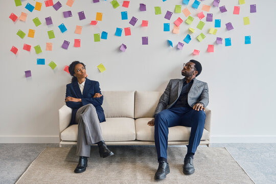 Man and woman sit on a couch looking at sticky notes on the wall