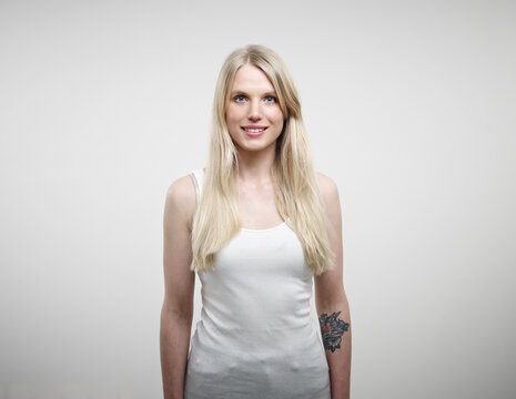 Portrait of young woman standing against white background, smiling