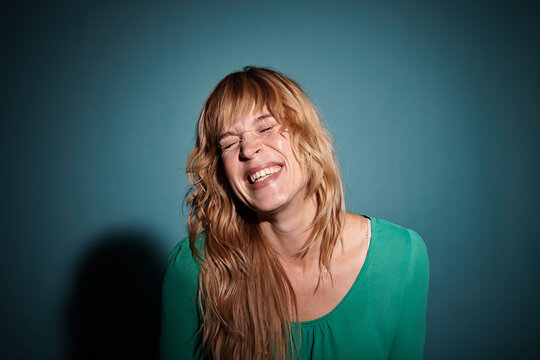 Portrait of laughing blond woman with closed eyes in front of blue background