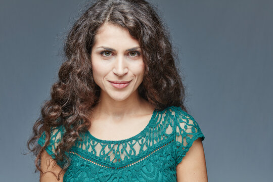 Portrait of smiling young woman with curly brown hair in front of grey background