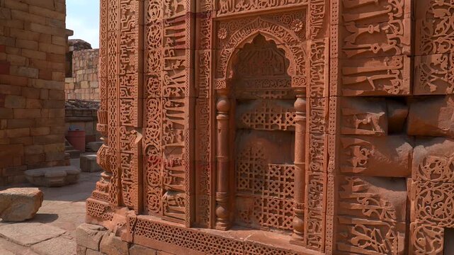 Close up shot of detailed Quranic calligraphy and geometric carvings on red sandstone walls at the Qutb Minar complex in New Delhi, India.