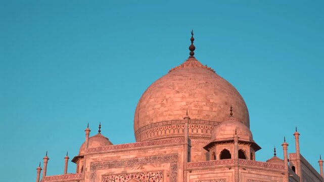 Static close up shot of the white marble central dome and chhatris of Taj Mahal glowing in golden hour light in Agra, India.