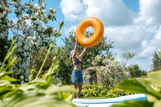 Woman holds orange inflatable ring in sunny summer garden