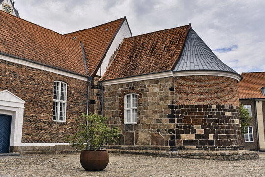 Varde, Denmark - 31 July 2026: View of St. Jacobi Kirke, a historic 12th-century church featuring massive granite block masonry, red tile roofs, and a rounded apse under a cloudy sky.