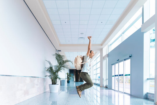 Excited male traveler celebrates vacation in modern airport corridor