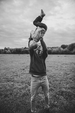 Black and white photo portrait of smiling dad throwing and turning little boy while son playing with dad outdoors in autumn field. Father and son having fun together during a walk in nature.
