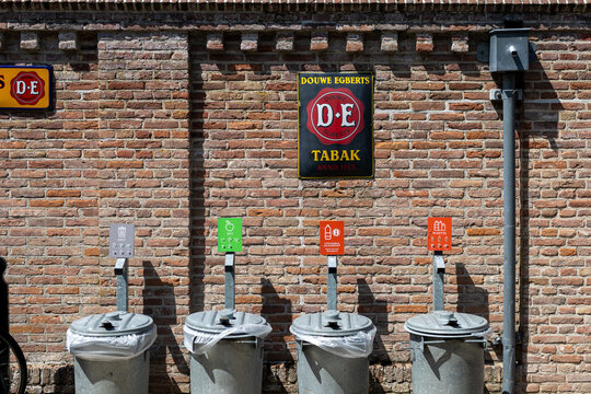 Enkhuizen, Netherlands - July 13, 2026: Waste separation bins for residual waste, organic waste, deposit bottles and plastic stand in front of a brick wall with a vintage Douwe Egberts tobacco sign.