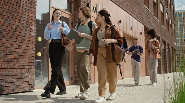 Diverse teenagers including Caucasian girls, Hispanic woman, Caucasian and Black men walking outside school building. Ideal for university recruitment and educational marketing campaigns