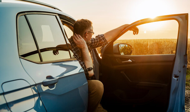 Pensive mature male driver taking a break and relaxing in vehicle during road trip at sundown. Side view.