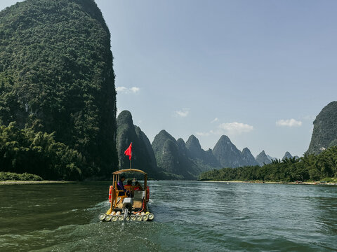 Guilin, China - 10 October 2024: View of a motorized bamboo raft cruising along the Li River in Yangshuo County, surrounded by iconic karst mountains under a clear blue sky.