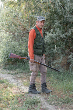 A hunter with a gun in camouflage clothing. A senior man with a gun, medium shot, searching for game.