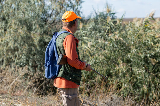 A hunter in camouflage clothing with a gun in his hands walks along the reeds.