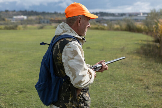 A hunter with a gun in camouflage clothing. A senior man with a gun, medium shot, searching for game.
