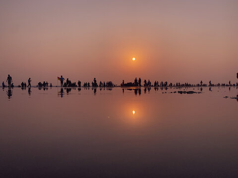Cox's Bazar, Chittagong Division, Bangladesh - 03 August 2026: View of silhouettes of people on wet sand at Cox's Bazar beach during sunset with sun reflecting on water.