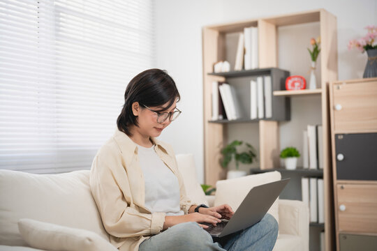 Woman Using Laptop in Cozy Home Office Setting with Bookshelf and Natural Light