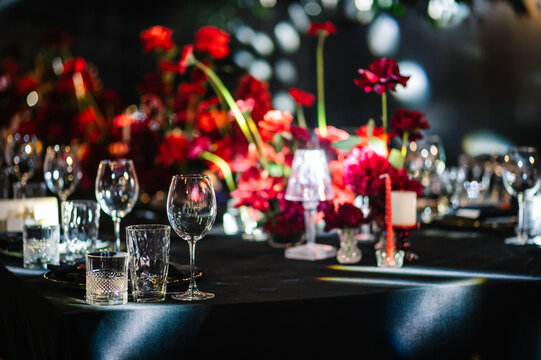 Elegant table setting with glassware and vibrant red floral centerpiece on a black banquet table. Sophisticated event setup, luxury style, perfect for wedding or celebration.