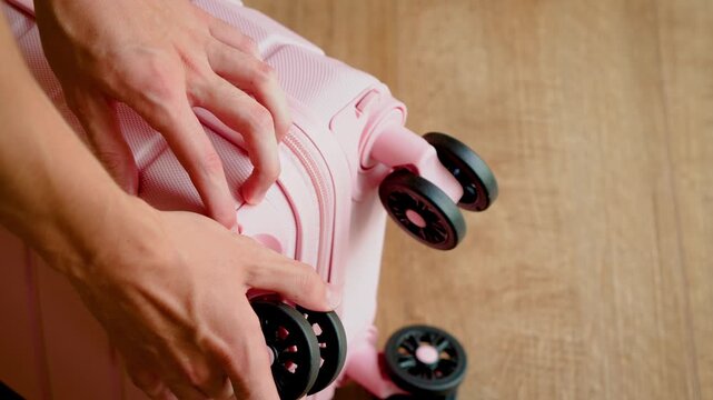 Male hands removing detachable wheels from pink suitcase for cabin baggage size compliance. Compact carry on luggage prepared for low cost airline travel. Budget flight hand luggage meeting baggage