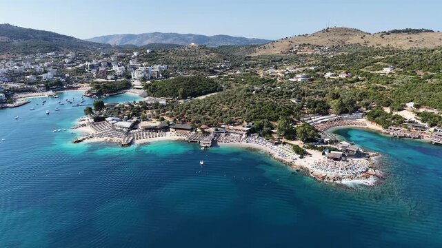 High angle drone shot of Saranda beachfront at dusk, luxury resort town in Albanian Riviera, Ionian sea. Saranda cityscape at night, pedestrian boulevard, public beach and coastal architecture, Albani