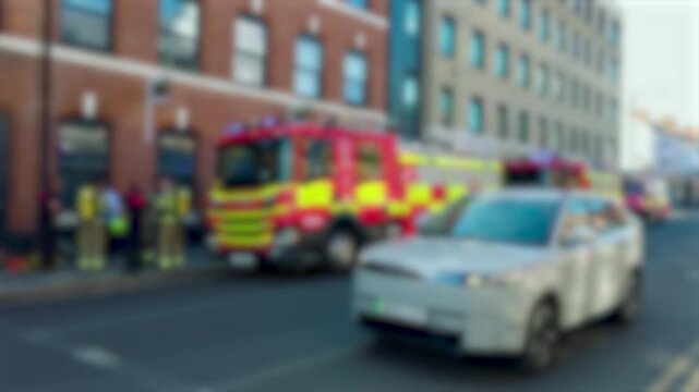Blurred fire engines with flashing emergency lights outside urban building. Firefighters responding to possible incident on city street. Accidents and disasters emergency response concept